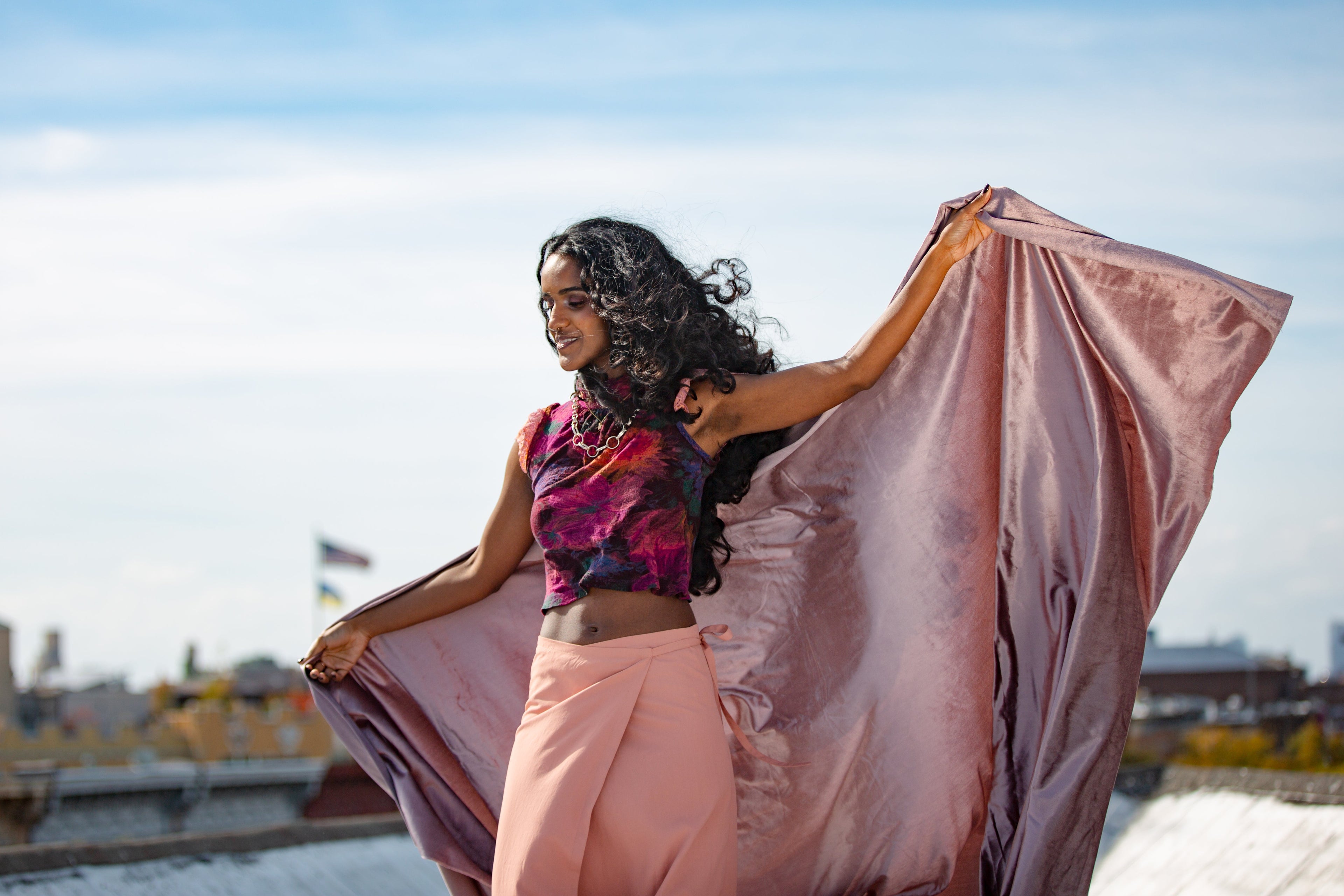 Woman in a pink outfit standing on a rooftop with a cityscape in the background